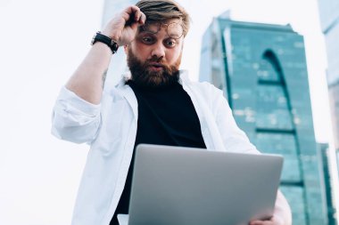 Heyecanlı erkek blogcu dışarıda içerik metni okurken dizüstü bilgisayar istatistiklerinden gelen şaşkınlığa uğramış, internetteki web sitesini izleyen hipster hayranı adam Netbook 'taki içerikten hayrete düşmüş.
