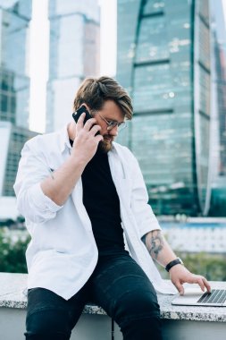 Genç bir erkek yeni uygulama ile akıllı telefon görüşmesi yapıyor, yetenekli bir iş adamı internette dolaşma konusunda operatöre açık dizüstü bilgisayarla arıyor.