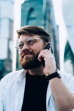 Göz koruması için optik gözlüklü beyaz bir adam şehir merkezinde uygulamayla cep telefonu sohbeti yapıyor. Arka planda gökdelenler, hareketlilik nesli kavramı var.