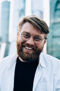 Şehir merkezinde boş zamanlarında kameraya gülümseyen, sokaklara neşe saçan mutlu bir adam için moda optik gözlüklü neşeli beyaz erkek portresi.