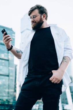 Gözlüklü beyaz adam cep telefonuyla sohbet okudu. 4G internete bağlandı. Arka planda gökdelenler var. Milenyum erkek yolcusu akıllı telefon kontrol rotasında navigasyon kullanıyor.