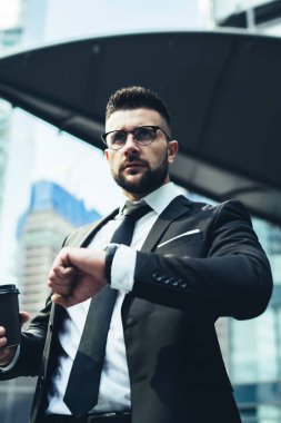 Aceleyle odaklanmış zarif bir yöneticinin bilek saatindeki kahve saatine bakıp dikkatle caddeye bakmasından.