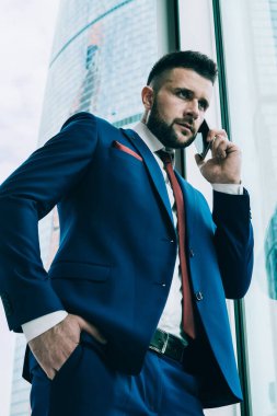 Aşağıdan iyi giyimli bir adam telefonda iş görüşmesi yaparken çağdaş ofisin penceresinin önünde el ele durur.