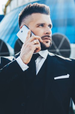 Resmi olarak giyinen ciddi bir erkek tüccar şirket ortağına dışarıda dururken şirket konferansı hakkında konuştuğu ve cep telefonunda gezinen internet bağlantısı kullandığı için çağrı yapıyor.
