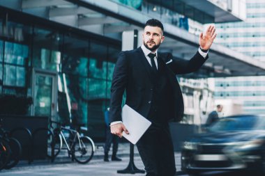 Taksi yakalamak için yaya geçidi boyunca el sallayan ve finans bölgesindeki şirket toplantısına ya da konferansa zamanında gelen, resmi olarak giyinmiş, dizüstü bilgisayarlı bir erkek yönetmen.