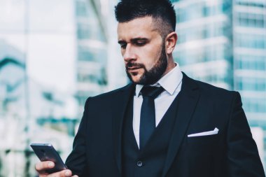 Moda kıyafetleri içinde, açık havada cep telefonu kullanan genç bir yönetici şık takım elbiseli kendine güvenen bir işadamı şehir merkezindeki 4G internete bağlı akıllı telefondan mesaj gönderiyor.