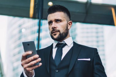 Modern şehrin caddesinde durup akıllı telefonları karıştırırken elinde tablet taşıyan ve gözlerini kaçıran takım elbiseli ciddi bir adamın alçak açısı.