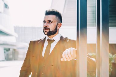 Modern şehir caddesinde güneşli bir günde direğe yaslanırken tabletle bakan zeki sakallı bir yönetici.