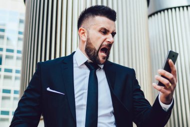 Manyak erkek girişimci, Megalopolis 'in finans bölgesindeki akıllı telefon cihazına bağırarak işletme sorunlarını çözmede sorun yaşıyor, mutsuz bir adam mobil cihaza bağırıyor.