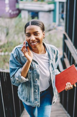 Kot pantolon giymiş neşeli Afro-Amerikan hippi kız portresi. Dışarıda kameraya gülümserken akıllı telefondan arıyor. Cep telefonuyla konuşan koyu tenli genç adam.