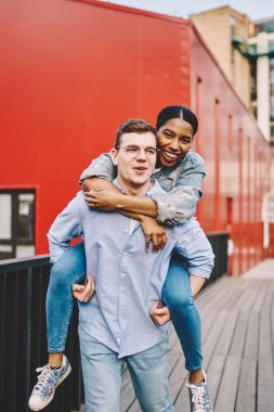 Neşeli romantik çiftin portresi açık havada dinleniyor, eğlenceli, beyaz bir adam esmer tenli sevgilisini sırtında gezdiriyor ve boş zamanlarında mutlu oluyor.