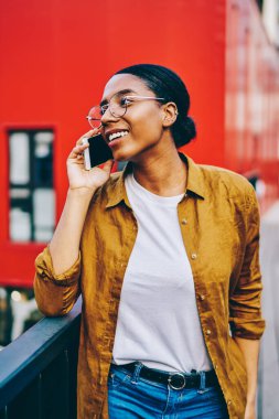 Gülümseyen koyu tenli gözlüklü hippi kız cep telefonuyla konuşarak gezen gezici aramalar için gümrük vergilerinden memnun, Afro-Amerikalı kadın akıllı telefonuyla sokakta sohbet ediyor.