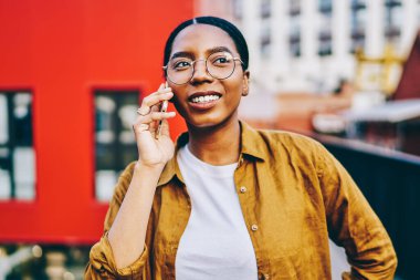Gözlüklü, gülümseyen Afro-Amerikan kadın dışarıda cep telefonuyla konuşuyor, pozitif esmer tenli hippi kız uluslararası akıllı telefon görüşmesi yapıyor.