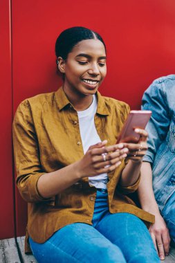 Neşeli hippi kız ve erkek sokakta oturup eğlenirken, Afro-Amerikan kadın akıllı telefondan sosyal ağlardan komik bilgiler okuyor ve erkek arkadaşıyla konuşuyor.