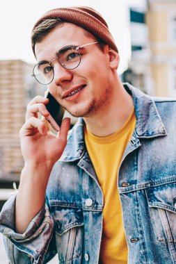 Giyim kuşamında ve gözlüklü genç yakışıklı hippi, gümrük vergileri hakkında operatörle cep telefonu kullanıyor, Kafkas asıllı bir erkek, gezici bir arkadaşla akıllı telefon görüşmesi yapıyor.