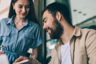 Düşük açılı etnik adam gülümseyen ve kadın iş arkadaşına not defterinde işaret eden sokak kafesinde oturup serbest iş yapan