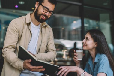 Düşük açılı etnik adam, uzaktan kumandalı bir iş yaparken içki içen bir kadına bilgi veriyor.