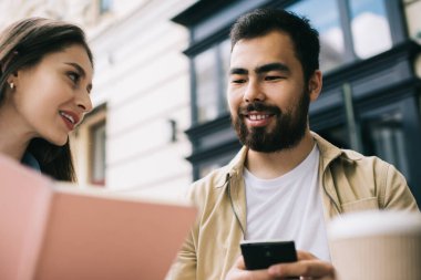 Düşük açılı genç bayan notlar gösteriyor. Şehir sokaklarında uzaktan kumandayla iş yaparken sakallı etnik meslektaşlarına veriler veriyor.