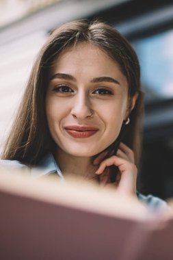 İçeriğin altında siyah saçlı kadın keşif kitabından gülümseyen ve kameraya bakan şehir caddesindeki bulanık arka plandaki binaya bakan.