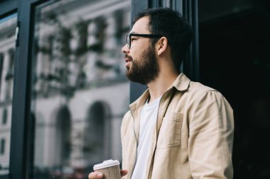 Kendine güveni tam, bej ceketli, gözlüklü, elinde laptopuyla kahve dükkanından çıkarken elinde kahve bardağıyla gezen...