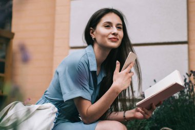 Akıllı telefonu ve planlayıcısı olan şık genç bir kadın elinde çiçeklerle sepetlerin yanında oturup şehir sokaklarında ders çalışırken gözlerini kaçırıyor.