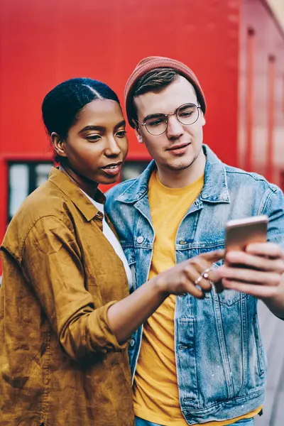 Son moda giyinmiş çok ırklı çift, şehirdeki ilgi alanlarını cep telefonuyla aramak için yeni uygulamaları kontrol ediyor, erkek ve kadın milenyum hipsterleri sosyal ağdan haberleri akıllı telefondan okuyorlar.