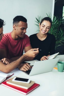 Gündelik giysiler içinde çok ırklı zeki bir grup dizüstü bilgisayarla masada oturuyor akıllı telefonları modern ışık yaratıcı çalışma alanına yerleştiriyor.