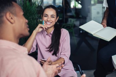 Ofis içi dostça sohbetler sırasında giyinmiş neşeli, çok kültürlü erkek ve bayan meslektaşlar birlikte çalışma projesinde çalışan pozitif hipster erkekler.