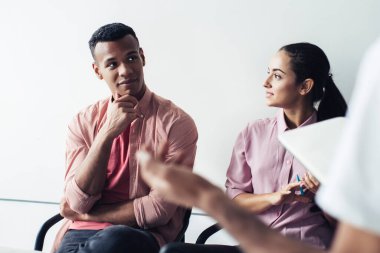 Çok ırklı, entellektüel, gündelik giysiler içindeki iş arkadaşları akıllı telefonlar ve bir fincan kahveyle modern, aydınlık ofis çalışma alanında oturuyorlar.