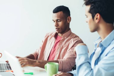 Gelişigüzel giyinen yetenekli erkek programcılar, ofis içi 4G kablosuz internete bağlı dizüstü bilgisayardaki yeni uygulama için tasarım üzerinde işbirliği yapıyorlar.