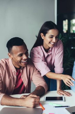 Ofiste çalışırken gülen yetenekli pazarlamacılar modern netbook 'taki internet tarayıcıları, neşeli erkek ve kadın çalışanlar iş yerinde takım çalışmasından ve arkadaşlıktan keyif alıyorlar.