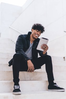 Mutlu Latin hipster adam şehir merdivenlerinde dinleniyor. Haberleri okuyor ve dijital tabletle komik bilgilere bakıyor. Kablosuz internet bağlantısı var.