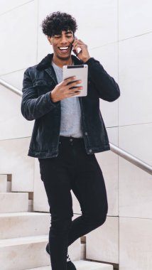 Moda kıyafetleri giymiş neşeli Latin adam komik içerikli e-posta alırken şaka tartışmak için arkadaşça bir telefon görüşmesi yapıyor, modern aletleri kullanan hippi adam dışarıda.