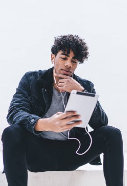 Dijital tabletli düşünceli bir adam, elektronik kulaklıklardan müzik şarkıları dinlerken sosyal web sitesinde sanal iletişim kuruyor, kulaklıklarda Latino nesli yayınlama üzerine kafa yoruyor.