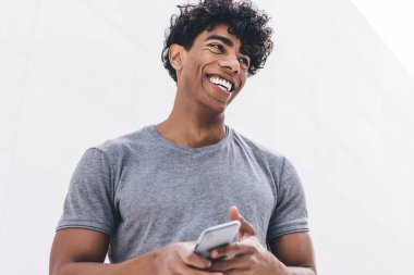 Elinde modern cep telefonu cihazı olan neşeli hippi adamın elinde komik bir e-posta mesajıyla gülüyor. Dijital cihazlı bir adam şehir ortamında gülümsüyor.