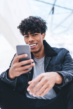 Şehir merkezinde dinlenen neşeli hipster adamın portresi ve hızlı internet bağlantısı olan akıllı telefon aygıtı, sohbet etmek için cep telefonu tutan pozitif milenyum insanı.