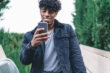 Şehre yürüyen merdivenden inen mutlu hipster adamı takipçilerle çevrimiçi iletişim kurmak için modern cep telefonu aygıtını kullanıyor. Sosyal sitede mesajlaşırken yakışıklı bir erkek blogger ağı kuruyor.