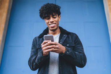 Günlük şık kıyafetler giymiş mutlu bir adam telefon ve sosyal siteye medya dosyaları paylaşmak için ağ kurmaktan keyif alıyor, milenyum erkek blogcu cep telefonu içeriği web sayfasından komik haberler okuyor