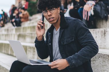 Moda kıyafetli tefekkür adamı, modern dizüstü bilgisayarla iş projesinin detaylarını tartışan uluslararası bir cep telefonu çağrısı aldı. Düşünceli erkek dijital göçebe, gezinen 4G kullanıyor.