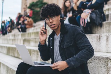 Moda kıyafetli tefekkür adamı, modern dizüstü bilgisayarla iş projesinin detaylarını tartışan uluslararası bir cep telefonu çağrısı aldı. Düşünceli erkek dijital göçebe, gezinen 4G kullanıyor.