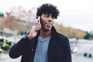 Mutlu Latin erkek turist, internet üzerinden iletişim kurmak için cep telefonu başvurusu yapıyor. Neşeli, modaya uygun giyinmiş hipster, uluslararası gezgin bağlantısıyla telefon ediyor.