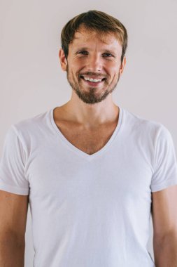 Modayı takip eden beyaz tişörtlü neşeli bir erkek portresi marka adı ya da etiketi için fotokopi alanı olan mutlu sakallı hippi adam duvarın arkasında kameraya bakıyor.