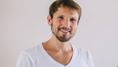 İnternet günlüğü için cep telefonu cihazını tutan genç dijital adamın yarım boy portresi ve boş zamanlarında kameraya gülümsemesi, beyaz tişörtlü, boş kopya alanı olan neşeli sakallı bir erkek.