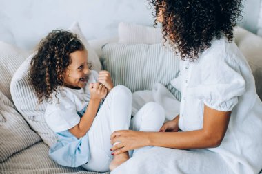 Çekici bir kız ve anne gibi kıvırcık saçlı rahat bir kanepede sarılıp birlikte vakit geçiriyorlar ve eğleniyorlar.