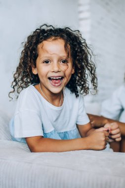 Sevimli, küçük bir kız. Annesiyle evde rahat bir kanepede oturup birlikte vakit geçirirken gülüyor ve kameraya bakıyor.