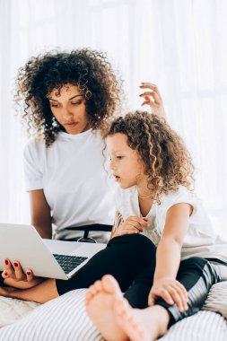 Pencere kenarındaki yastıklarda takılan ve boş zamanlarında birlikte dizüstü bilgisayar kullanan küçük kızı olan çekici bir etnik kadın.