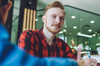 İçerde arkadaşlarıyla otururken kameraya bakan zeki bir erkek öğrencinin portresi. Sıradan giyinmiş, ders kitabı ödevi yapan ve ders kitabı okuyan zeki bir beyaz adam.