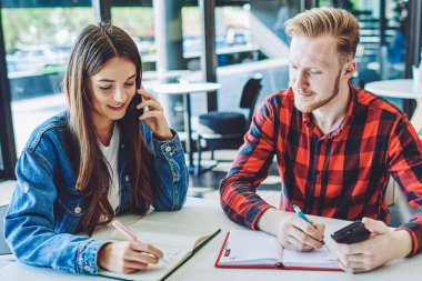 Mutlu gülümseyen hippi kız, üniversite sınavına hazırlanırken yanında oturan erkek arkadaşıyla canlı iletişimi görmezden gelerek olumlu bir akıllı telefon konuşması yapıyor.