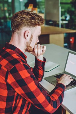 Yoğunlaşmış erkek, iş arkadaşlarıyla birlikte masada oturan reklam metni için boş ekranı olan dizüstü bilgisayarı programlamak için kablosuz internet bağlantısını kullanarak kapalı alanda çalışıyor.