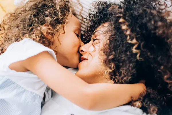 Evinde kıvırcık saçları olan, yatakta sarılıp şefkatle öpüşen sevimli, benzer bir kızı olan çekici bir etnik kadından.